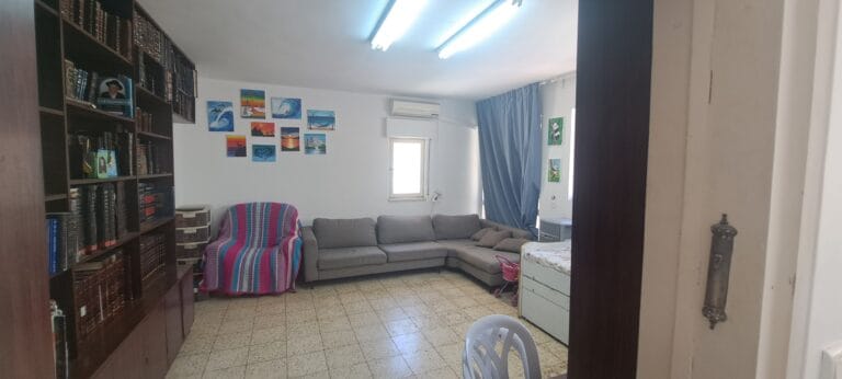 Wide view of the living room, bookshelves and gray sofa in the Hakalir 4-bedroom apartment in Rechavia.