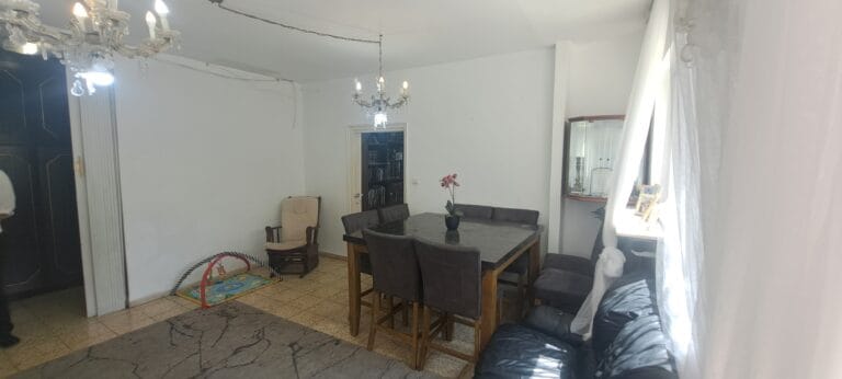 Wide view of the dining table, sitting area and curtained windows in the Hakalir 4-bedroom Rechavia apartment.