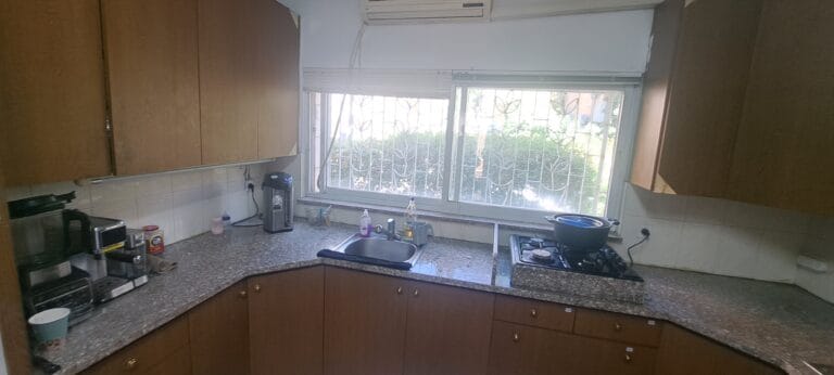 Kitchen with wooden cabinets, counters and a large window in the Hakalir 4-bedroom apartment, Rechavia, Jerusalem.