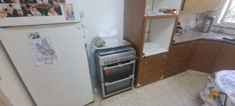 Freestanding stove and refrigerator beside wooden kitchen cabinets in the Hakalir 4-bedroom Rechavia apartment.