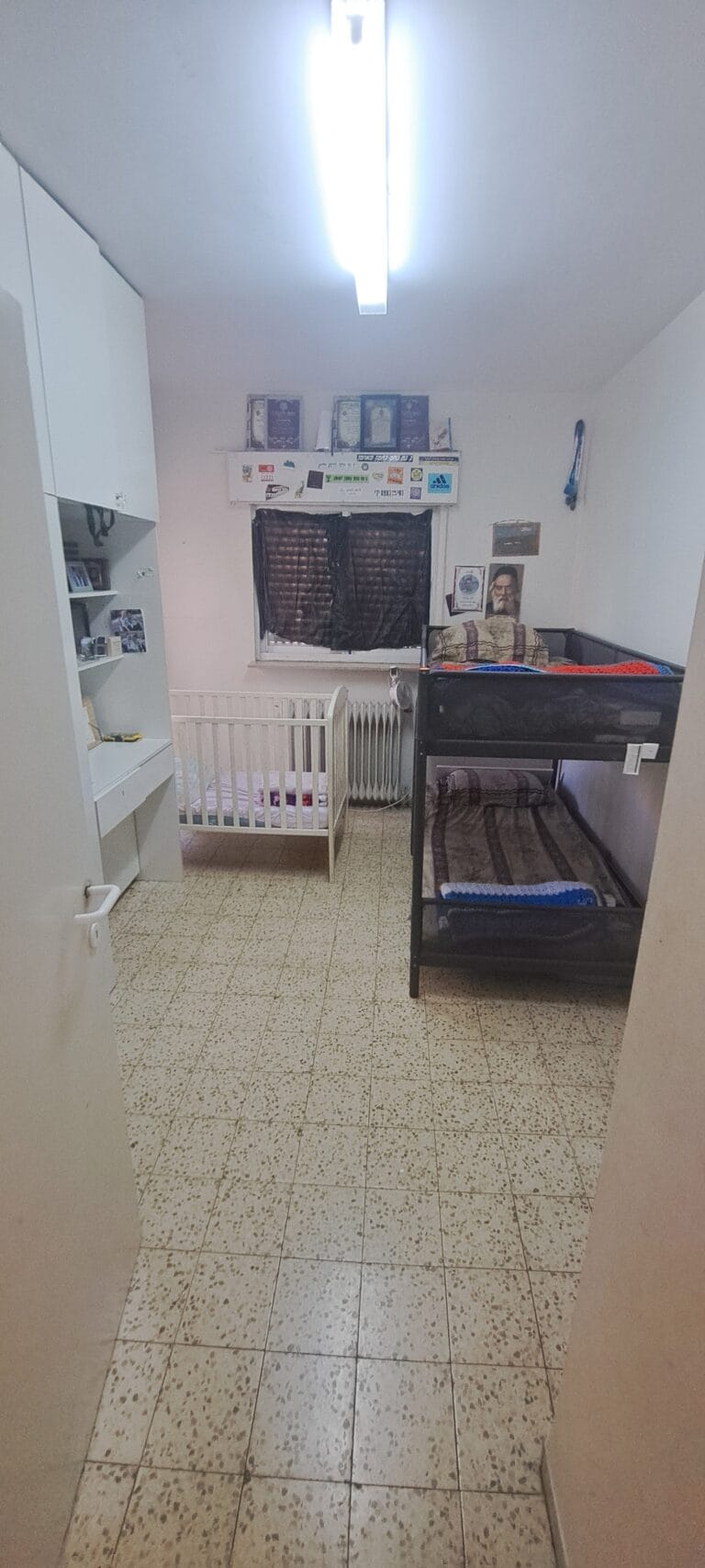 Bedroom with dark bunk beds, a crib and built-in storage in the Hakalir 4-bedroom apartment in Rechavia.