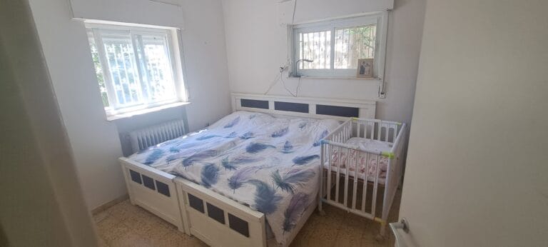 Bedroom with beds, a crib and a window in the Hakalir 4-bedroom apartment in Rechavia, Jerusalem.