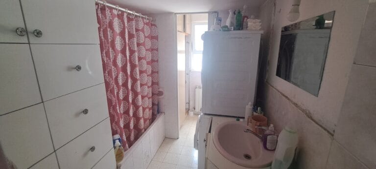Bathroom with bathtub, pink shower curtain, toilet and mirrored cabinet in the Hakalir 4-bedroom Rechavia apartment.