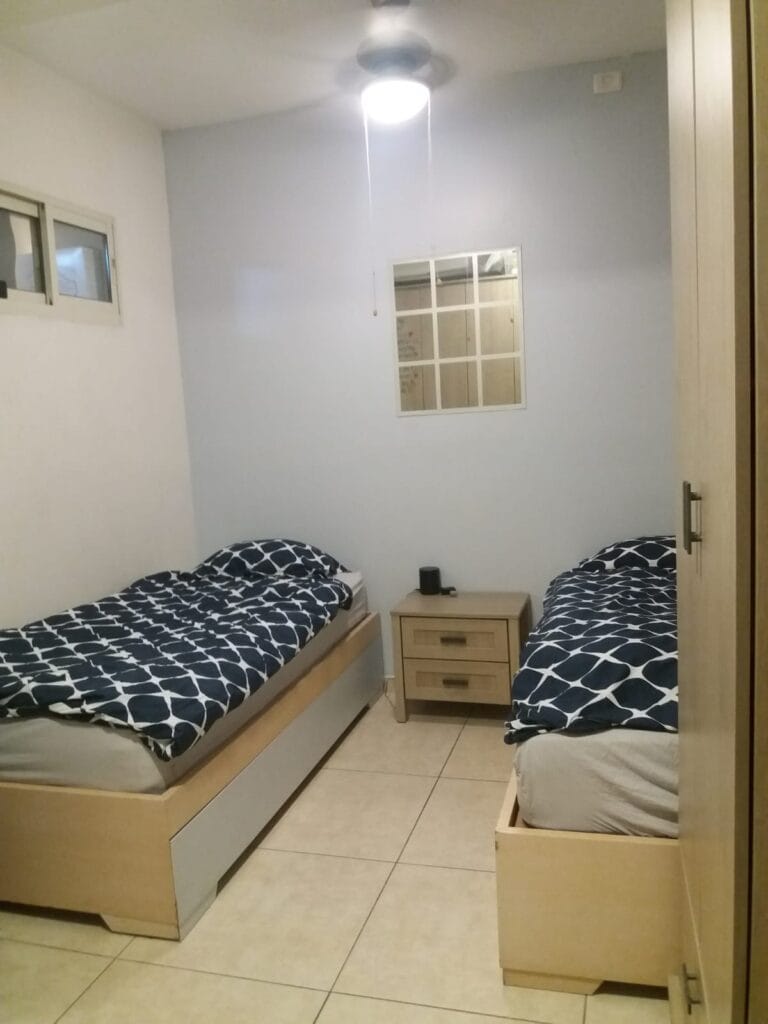 Twin bedroom with light wood bed frames, navy bedding, wardrobe and ceiling fan at Ramban Giant Sukkah Apartment, Jerusalem