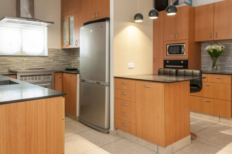 Wood-tone kitchen with refrigerator-freezer, range cooker, additional oven, microwave and breakfast counter at Ramban Giant Sukkah Apartment, Jerusalem