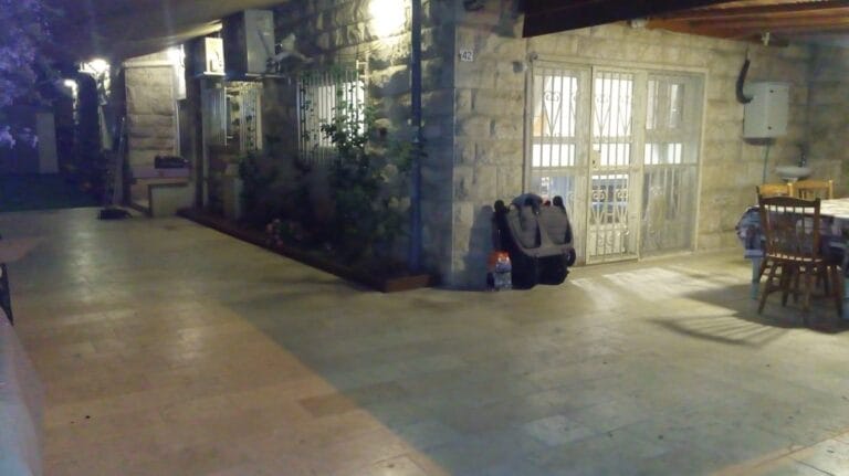 Illuminated courtyard outside the living-room doors with outdoor dining furniture at Ramban Giant Sukkah Apartment, Jerusalem