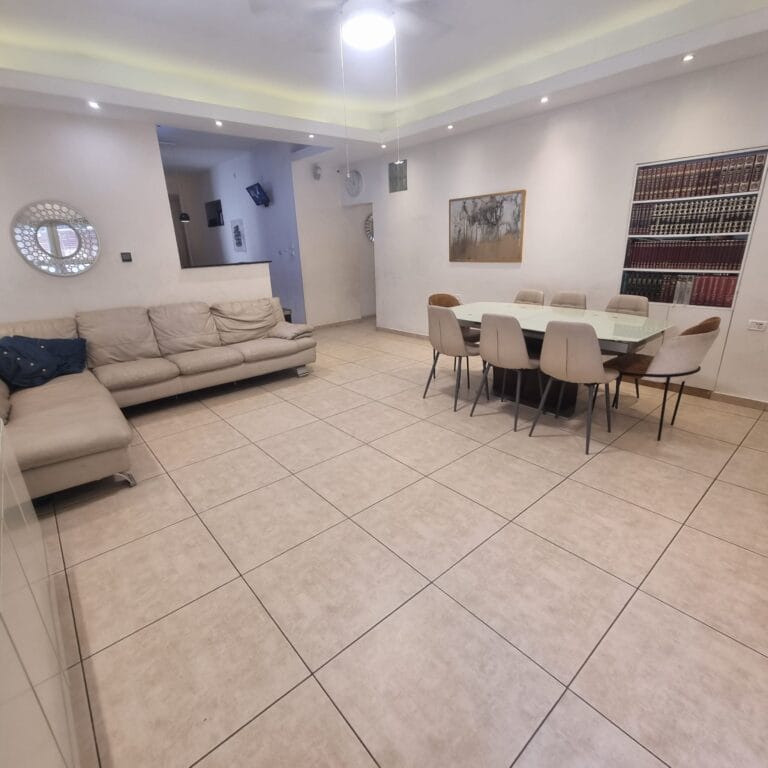 Living and dining room with a cream corner sofa and an eight-chair dining table at Ramban Giant Sukkah Apartment, Jerusalem