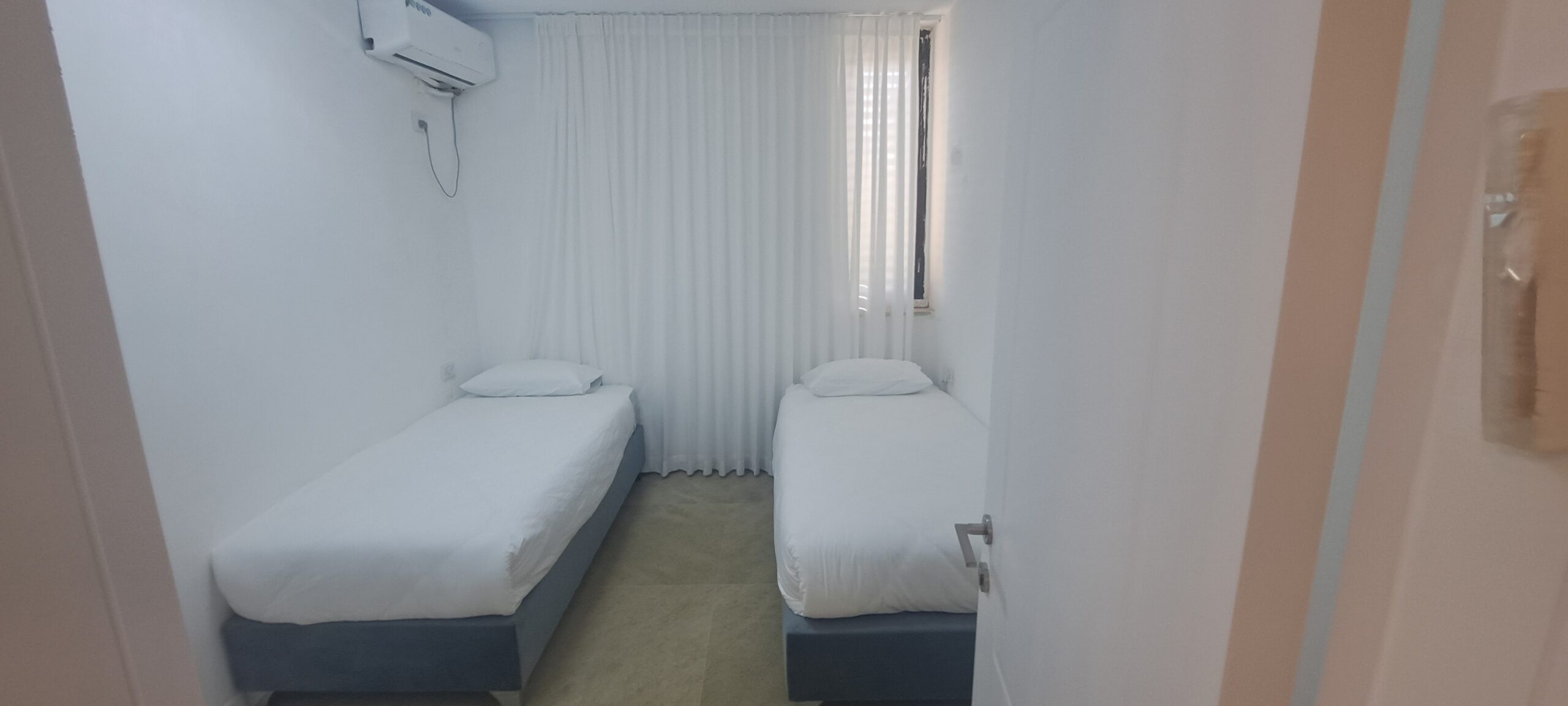 Twin bedroom with two separate beds, curtains and air conditioning at Wolfson Villa in Jerusalem.