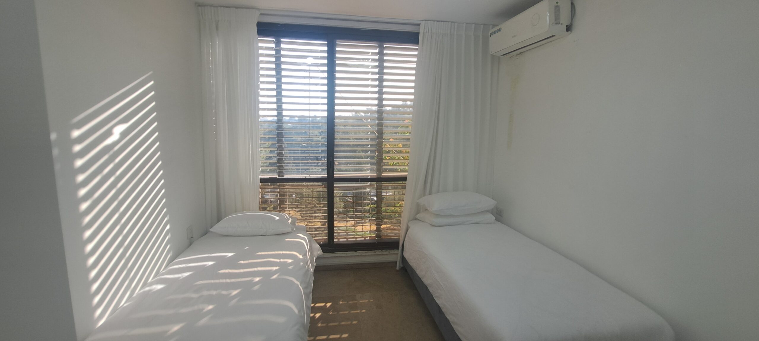 Bright twin bedroom with two separate beds and a park-facing window at Wolfson Villa in Jerusalem.