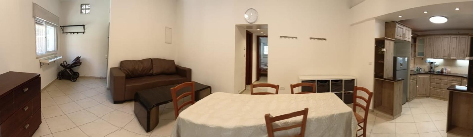 Panoramic view of the sofa, coffee table, dining table and open kitchen at Ibn Shaprut Apartment #2