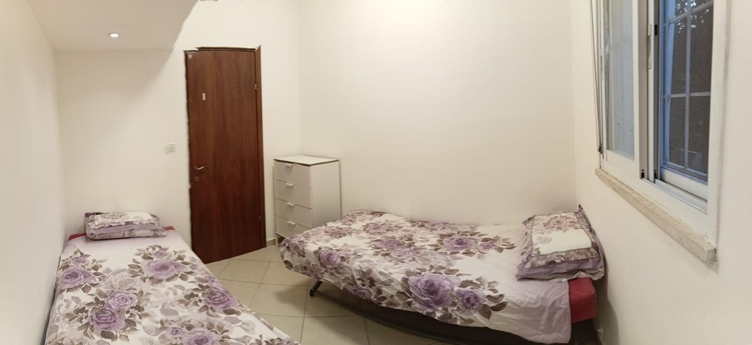 Two single beds with floral bedding, a white drawer unit and a window at Ibn Shaprut Apartment #2