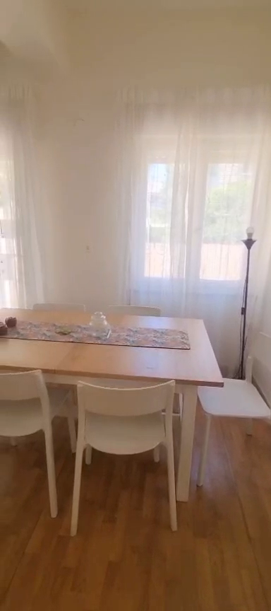 Wooden dining table with white chairs beside sheer curtains in the Ibn Shaprut apartment.