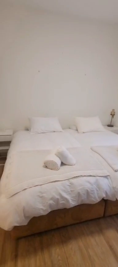 Two beds placed together with white bedding and rolled towels in the Ibn Shaprut apartment.