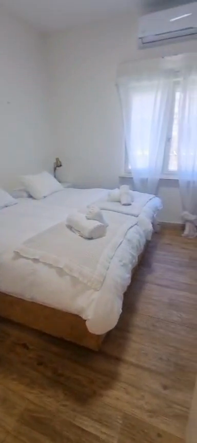 Main bedroom with white bedding, rolled towels, sheer curtains and air conditioning in the Ibn Shaprut apartment.