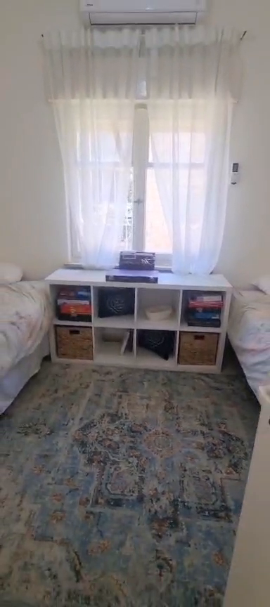 Twin bedroom with beds on opposite walls, cubby storage, a patterned rug and a window in the Ibn Shaprut apartment.