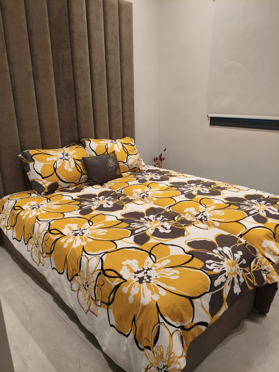 Beds with yellow floral bedding and a tall upholstered headboard in the Ramban Rechavia apartment.