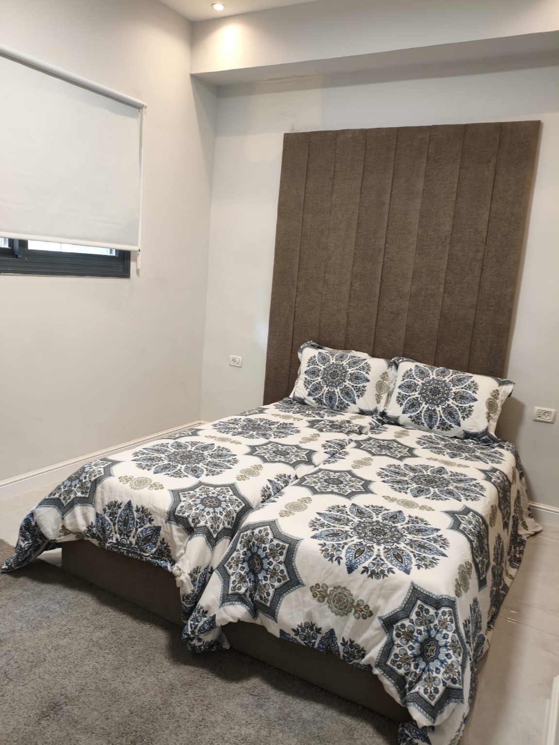 Twin beds with blue-and-white patterned bedding and a tall upholstered headboard in the Ramban Rechavia apartment.